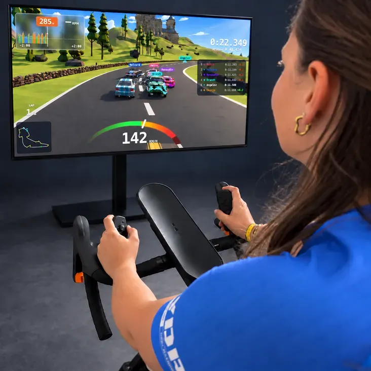A rider on a smart trainer, a controller in each hand, racing others live in Split Racing on a big screen