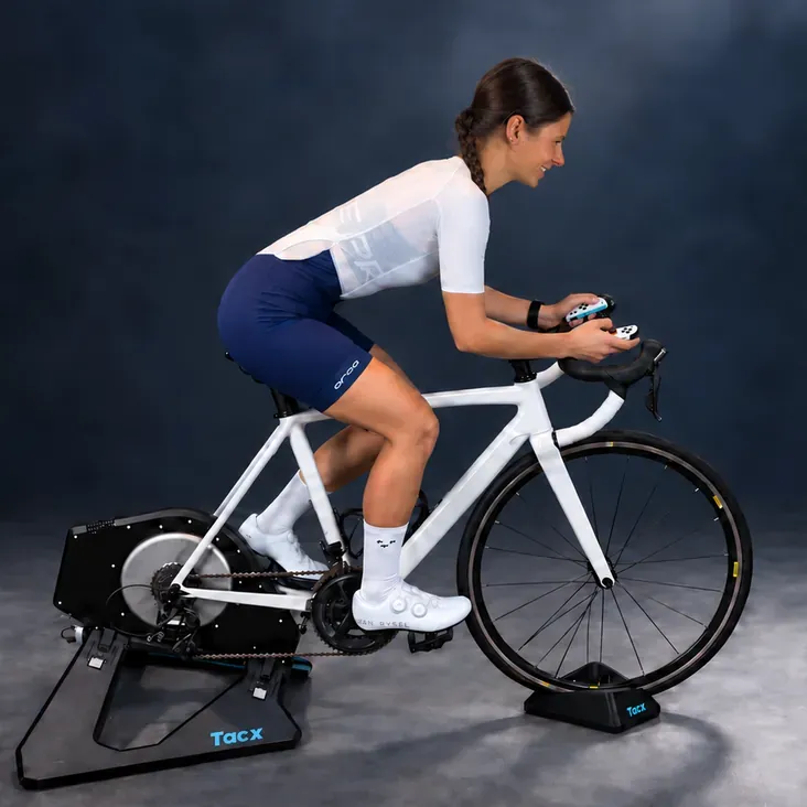 A rider pedalling a road bike on a Tacx smart trainer, a Switch Joy-Con in each hand