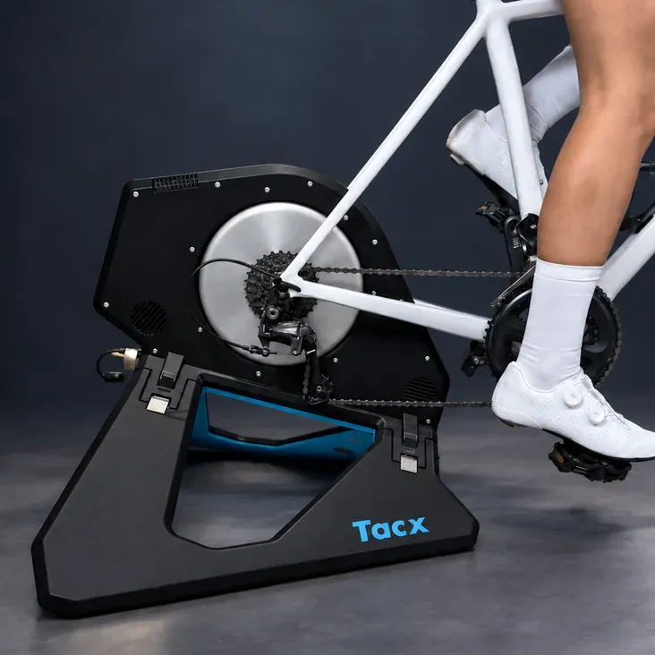 A road bike mounted on a direct-drive smart trainer, a rider's foot clipped into the pedal